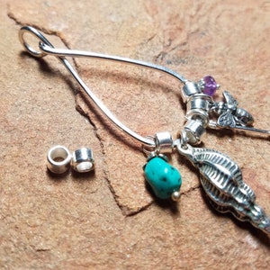 May include: A silver charm bracelet with a variety of charms, including a turquoise stone, a purple stone, a bee, and a seashell. The bracelet is made of silver and has a delicate design.