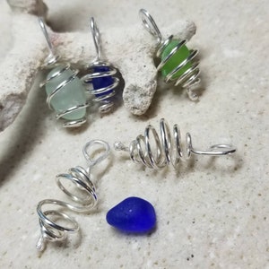 May include: Five silver wire wrapped sea glass pendants. The sea glass is in various colors, including blue, green, and light blue. The pendants are all in a spiral shape.