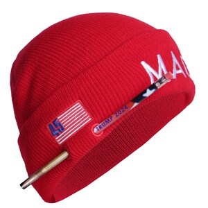 May include: Red knit beanie with a white "MAGA" embroidered on the side, a small American flag patch, and a gold-colored pen with "TRUMP 2024" written on it.