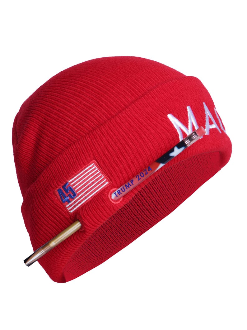 May include: Red knit beanie with a white "MAGA" embroidered on the side, a small American flag patch, and a gold-colored pen with "TRUMP 2024" written on it.