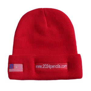 May include: Red knit beanie with a white embroidered American flag and the text "www.2024pencils.com" on the front.