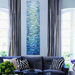 May include: Abstract painting with a vertical design of blue, green, and white paint. The painting is displayed on a wall in a living room setting.