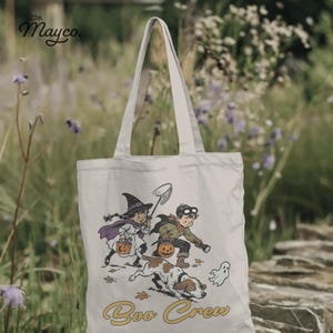 May include: A cream-colored canvas tote bag featuring a vintage-style illustration of a child dressed as a witch and another as an explorer with a dog, a small ghost, and the text "Boo Crew" printed in yellow. The brand "22th Mayco." is visible.