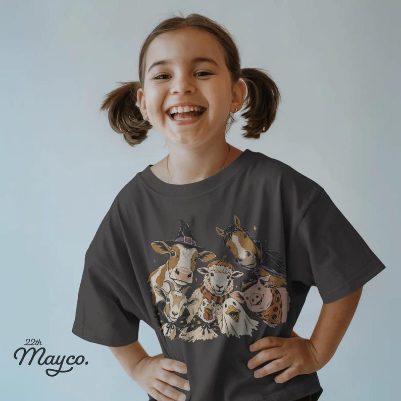 May include: A dark gray short-sleeve t-shirt featuring a graphic print of a cow wearing a witch hat, a sheep, a horse, a goat, a pig, and a duck. The text 22th Mayco. is printed in black in the lower left corner of the shirt design.