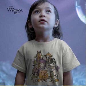 K&ouml;nnte beinhalten: Ein hellgraues T-Shirt mit einer grafischen Illustration verschiedener Bauernhoftiere in Halloween-Kost&uuml;men, darunter ein Pferd, eine Kuh, eine Ziege, ein Schaf, ein Schwein und ein Huhn. Der Text 22th Mayco. steht oben links im Bild.