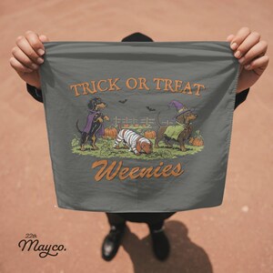 May include: A dark gray fabric square featuring a graphic of three dachshunds in Halloween costumes among pumpkins. The text reads TRICK OR TREAT at the top and Weenies at the bottom in orange lettering. The dogs are dressed as a vampire, a mummy, and a witch.