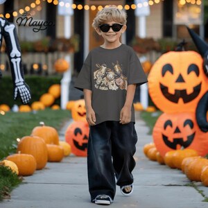 May include: A charcoal gray short-sleeve t-shirt featuring a graphic print of various farm animals wearing Halloween costumes, paired with loose-fitting dark denim jeans and black sunglasses. The shirt displays the text 22th Mayco.