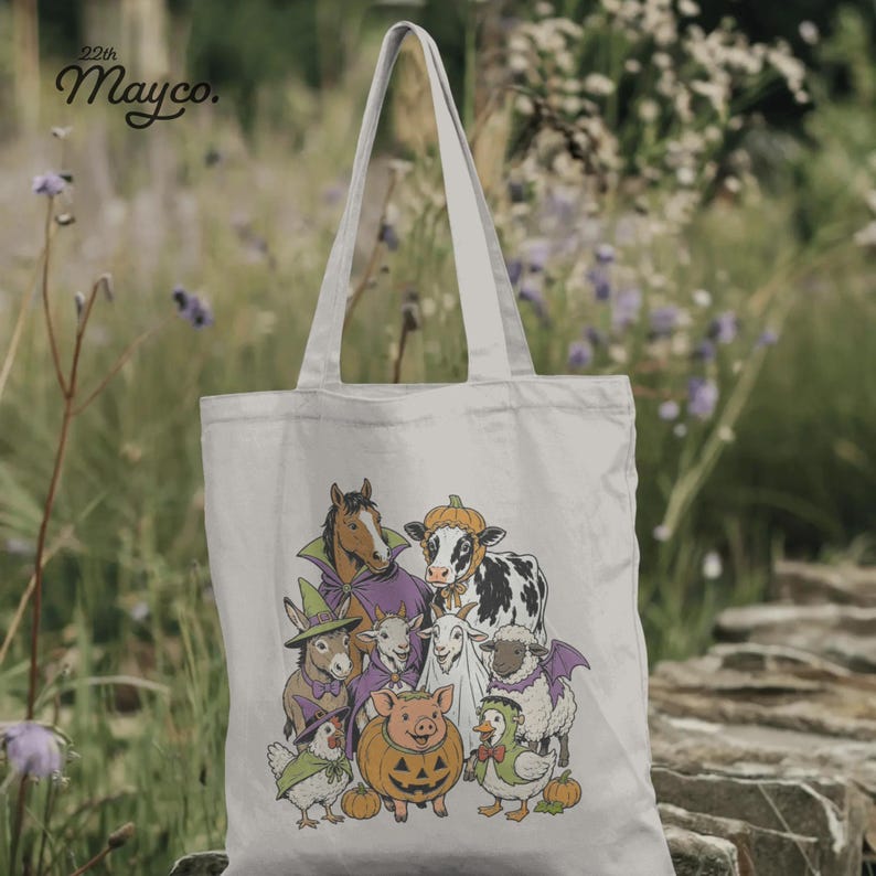 K&ouml;nnte beinhalten: Eine helle Stofftasche mit einer grafischen Illustration von Bauernhoftieren in Halloween-Kost&uuml;men, darunter ein Pferd, eine Kuh, ein Schwein, ein Schaf, eine Ziege und ein Huhn. Der Text 22th Mayco. ist in der oberen linken Ecke aufgedruckt.