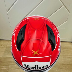 May include: A red motorcycle helmet with a white and gold Marlboro logo. The helmet has a black visor and black accents.