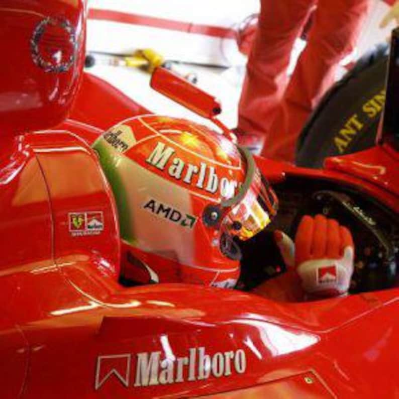 May include: A red race car with a driver wearing a red and white helmet with the word "Marlboro" on it. The car has a large "Marlboro" logo on the side.