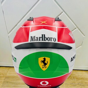 May include: A white, red, and green motorcycle helmet with a black visor. The helmet has the Marlboro logo, a Ferrari logo, and the Vodafone logo.