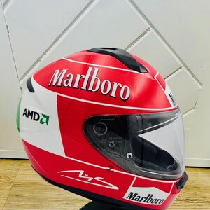 May include: A red, white, and green motorcycle helmet with a Marlboro logo on the side. The helmet has a clear visor and a black chin strap.