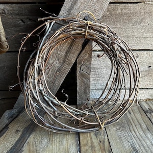 May include: A brown grapevine wreath, made of natural twigs, is tied together with twine. The wreath is circular and has a rustic appearance.
