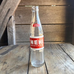 May include: A clear glass bottle with a red and white label that reads "Nehi" and "Contents: 10 Fl. Oz."
