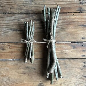 May include: Two bundles of natural wooden sticks tied with twine, arranged on a rustic wooden surface. The sticks vary in length and thickness, with a mix of light and dark brown tones. The twine adds a touch of rustic charm to the presentation.