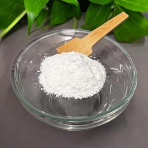 May include: A white powder in a clear glass bowl with a wooden scoop. The powder is a fine, white powder and is likely a baking ingredient.