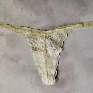May include: A delicate, off-white lace thong with a floral pattern.