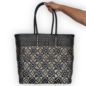 May include: A black and gold woven tote bag with a checkered pattern. The bag has two handles and is made of a sturdy material.