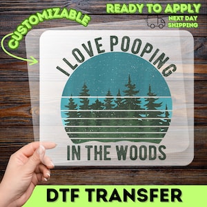 May include: A clear DTF transfer sheet featuring a circular graphic with a teal and green sunset background, a silhouette of pine trees, and the black text I LOVE POOPING IN THE WOODS arranged in a curved design above and below the forest scene.