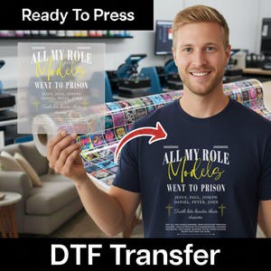 May include: A navy blue t-shirt featuring white and yellow text that reads: ALL MY ROLE Models WENT TO PRISON, JESUS, PAUL, JOSEPH, DANIEL, PETER, JOHN, Truth hits harder than dreams, and additional smaller text at the bottom.