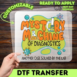 May include: A DTF transfer featuring the words "MYSTERY MACHINE OF DIAGNOSTICS" in orange, with science-themed illustrations. The design is on a clear background, with the words "CUSTOMIZABLE" and "READY TO APPLY" visible.