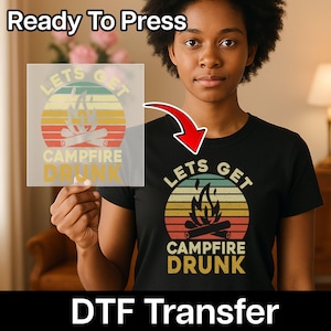 May include: Black t-shirt with a retro sunset design featuring a campfire graphic and the words "Lets Get Campfire Drunk". The image also shows a DTF transfer with the same design, ready to press.