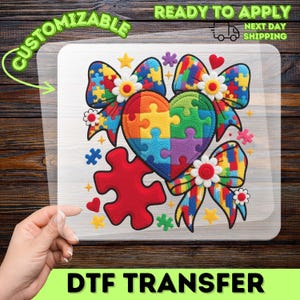 May include: A DTF transfer featuring a colorful puzzle heart, bows, and puzzle pieces. The design includes the text "CUSTOMIZABLE" and "READY TO APPLY NEXT DAY SHIPPING". The heart and bows are made of puzzle pieces.
