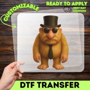 May include: A DTF transfer featuring a cartoon character with a top hat, round sunglasses, and a tie. The character is light brown with a serious expression. The transfer is labeled "Customizable" and "Ready to Apply".