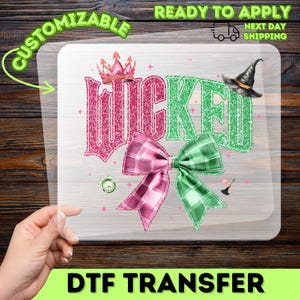 May include: A DTF transfer featuring the word "Wicked" in pink and green glitter, with a pink crown, a witch hat, and two plaid bows. The design is on a clear background with the words "Customizable" and "Ready to Apply" and a shipping icon.