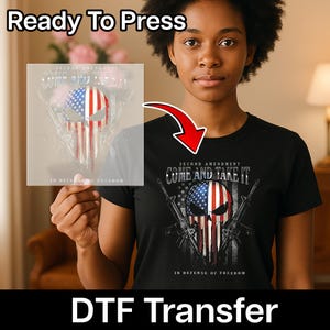 May include: Black t-shirt with a skull design featuring the American flag and the text "COME AND TAKE IT". The image also shows a DTF transfer with the same design, ready to press. The text "IN DEFENSE OF FREEDOM" is also visible.