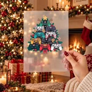 Op de afbeelding: Een doorschijnend vel met een grafische illustratie van een kerstboom opgebouwd uit diverse kleurrijke videogamecontrollers. De boom is bekroond met een gouden ster en versierd met kerstverlichting, rode bessen en een rode strik aan de onderkant.