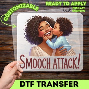 May include: DTF transfer featuring a cartoon illustration of a mother and child. The child is kissing the mother's cheek. The text "Smooch Attack!" is displayed below the image. The words "Customizable" and "Ready to Apply" are also present.