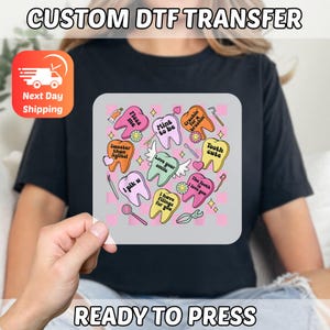 May include: A black t-shirt with a DTF transfer featuring colorful cartoon teeth with phrases like "Floss me" and "Tooth cute." The words "CUSTOM DTF TRANSFER" and "READY TO PRESS" are printed on the image.