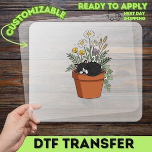 May include: A clear DTF transfer sheet featuring a graphic of a black and white cat curled up inside a terracotta-colored flower pot filled with various wildflowers, including daisies, yellow blossoms, and green foliage, with a white background.