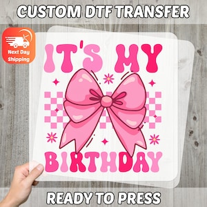 May include: A pink and white DTF transfer with the text "IT'S MY BIRTHDAY" and a large pink bow. The design includes a checkered background and floral accents. The words "READY TO PRESS" are at the bottom.
