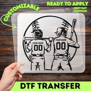 May include: A black and white DTF transfer featuring two baseball players with the text "YOUR NAME" and the number "00" on their jerseys. The design is set against a baseball and includes the words "CUSTOMIZABLE" and "READY TO APPLY".