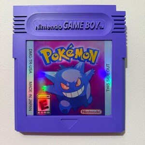 May include: A purple Nintendo Game Boy cartridge wall display featuring a holographic Pok&eacute;mon label with Gengar, the text Pok&eacute;mon, Nintendo GAME BOY, DMG-TR-USA, MADE IN JAPAN, THIS SIDE OUT, and an ESRB Everyone E rating symbol.