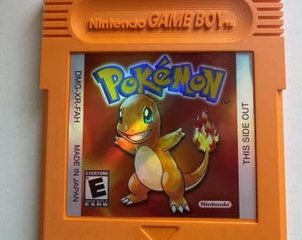 Puede incluir: Un cartucho de videojuego naranja para Nintendo Game Boy con una etiqueta que muestra el logotipo de Pokémon y una ilustración del personaje Charmander. La etiqueta incluye el texto DMG-XR-FAH, MADE IN JAPAN, THIS SIDE OUT y la clasificación ESRB E.