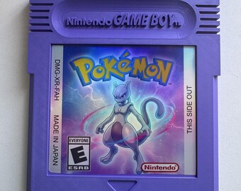 Puede incluir: Un cartucho de videojuego Nintendo Game Boy de color morado con una etiqueta holográfica que muestra el logotipo de Pokémon y una ilustración del personaje Mewtwo. La etiqueta incluye la clasificación ESRB E, el logo de Nintendo y el texto DMG-XR-FAH MADE IN JAPAN.