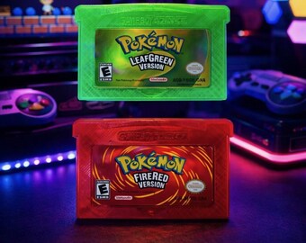 Puede incluir: Dos cartuchos de Game Boy Advance: uno verde con "Pokémon LeafGreen Version" y otro rojo con "Pokémon FireRed Version". Ambos cartuchos muestran la clasificación ESRB y la marca Nintendo. El fondo presenta equipos de juego.