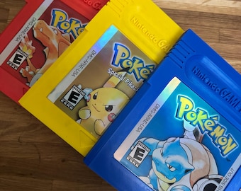 Puede incluir: Tres cartuchos de Pokemon Game Boy de colores. El cartucho rojo presenta a Charizard, el amarillo a Pikachu y el azul a Blastoise. Cada cartucho tiene el logo de Pokemon y la clasificación ESRB.