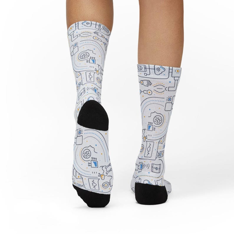 May include: White crew socks featuring a repeating pattern of blue, yellow, and grey abstract designs. The socks have black heels and toes. The design includes lines, dots, and various shapes.