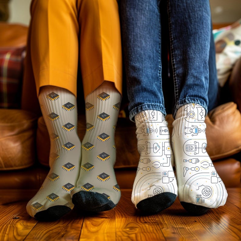 May include: Two pairs of socks with different designs. One pair is light grey with a repeating pattern of black and yellow AI chips. The other pair is white with a black and blue tech-themed design.