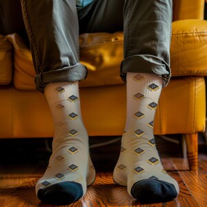 May include: Light beige socks featuring a repeating pattern of gold and black computer chip graphics. The socks have black heels and toes. The person wearing the socks is sitting on a yellow sofa.