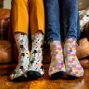 May include: A pair of socks with a repeating pattern of colorful cats. The socks are worn by a person wearing yellow pants. Another person is wearing blue jeans and socks with a repeating pattern of colorful squares with cat faces.