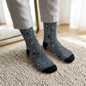 May include: A pair of crew-length socks featuring a dark charcoal gray base with a repeating white line pattern of interconnected circuit board pathways, small square microchips, and mechanical gear icons, finished with solid black toe and heel caps.