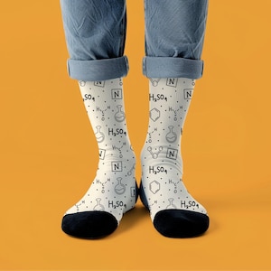 May include: White socks with black heels and toes, patterned with scientific diagrams and the chemical formula H2SO4. The socks are worn with blue jeans. The background is orange.