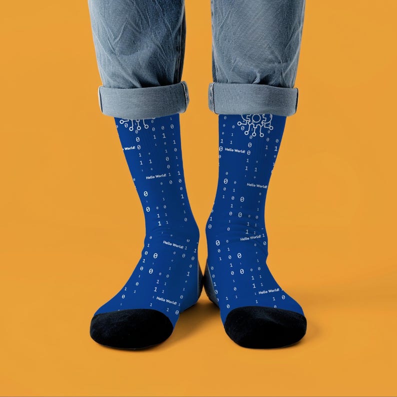 May include: A pair of blue socks with a pattern of white binary code and the text "Hello World!". The socks have black toes and heels. The socks are worn by a person wearing blue jeans.