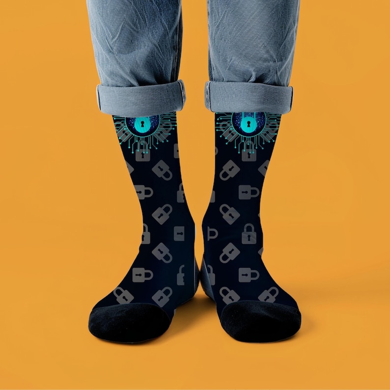 May include: Black socks with a cybersecurity design. The socks display a pattern of grey padlocks and a blue and teal lock graphic at the top. The socks are worn with blue jeans against an orange background.