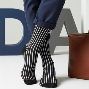 May include: Black and white striped socks with a red trim at the toe are worn with navy blue trousers. A brown leather briefcase is visible in the background. The socks have vertical stripes.